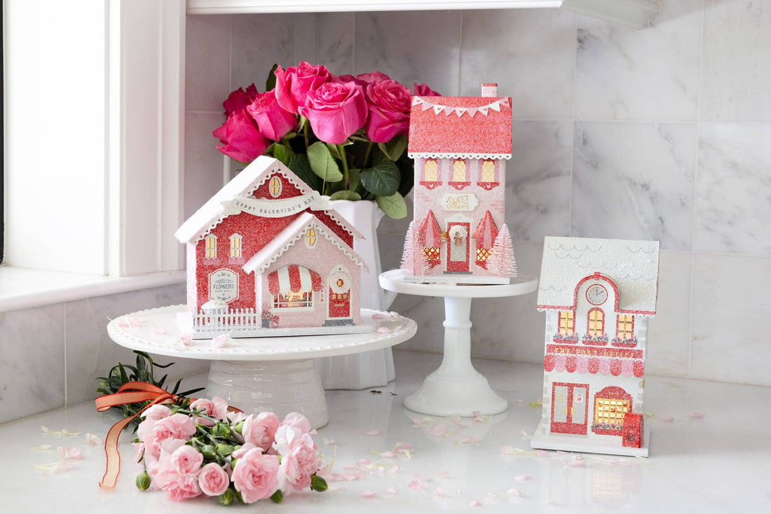 Decorative miniature houses on stands with pink roses on a marble surface.
