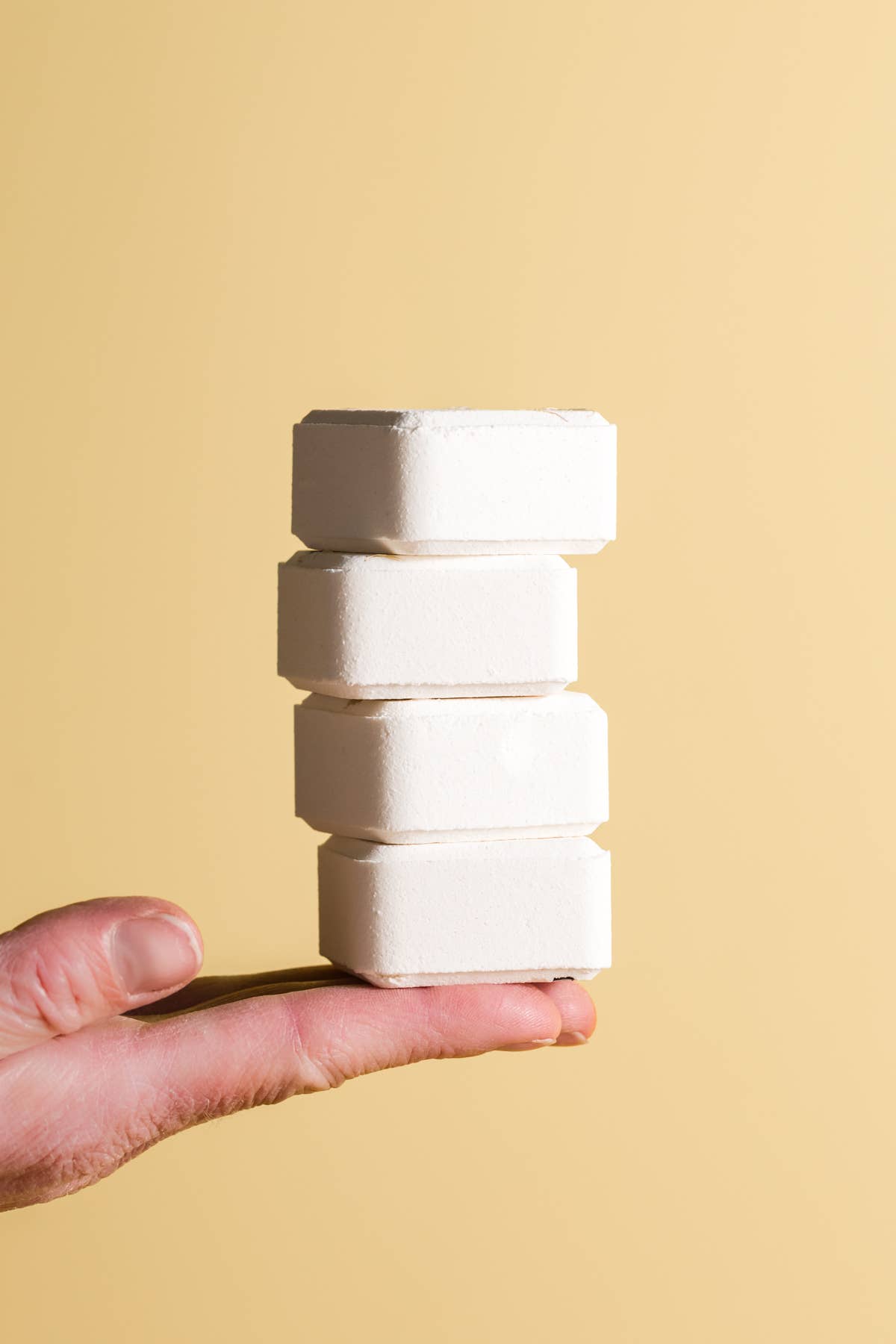 Hand holding a stack of white shower steamer blocks against a beige background