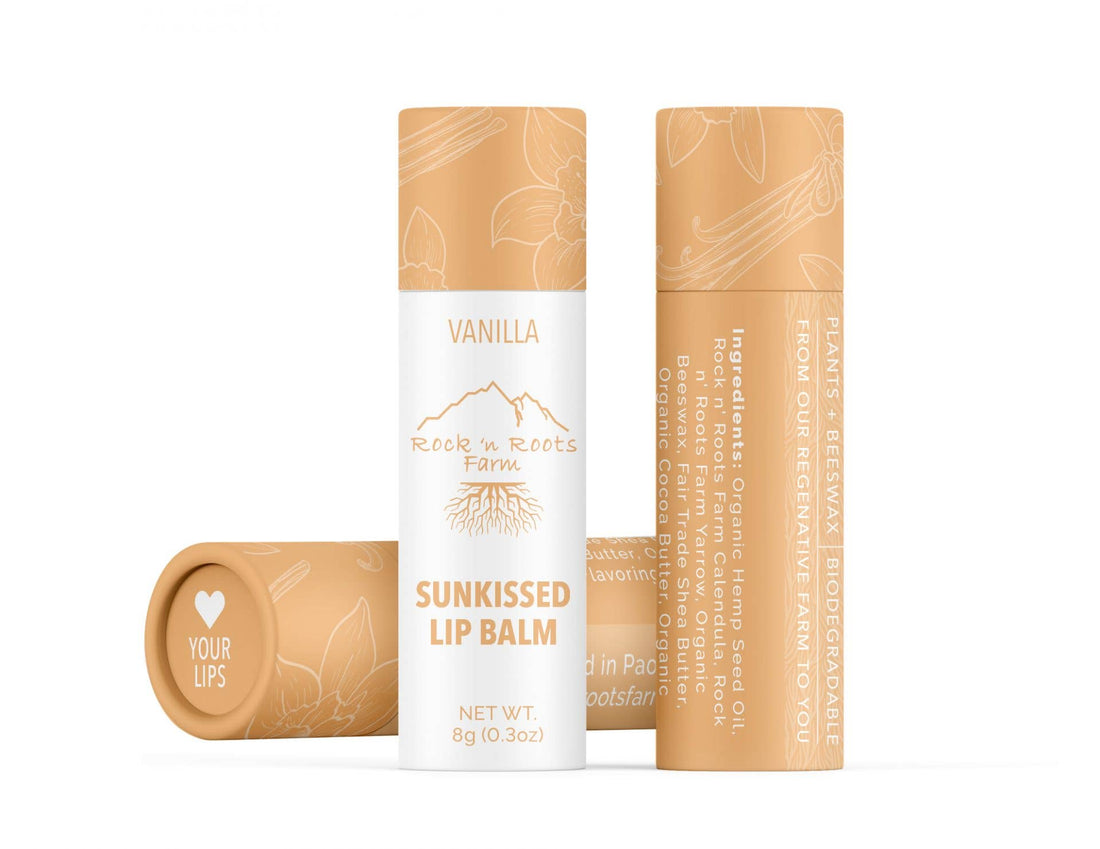 Two tubes of Sun Kissed Lip Balm, one standing upright and one on its side, with the lid of the latter tube showing. The packaging is beige with text and branding, and the flavor is indicated as Vanilla.