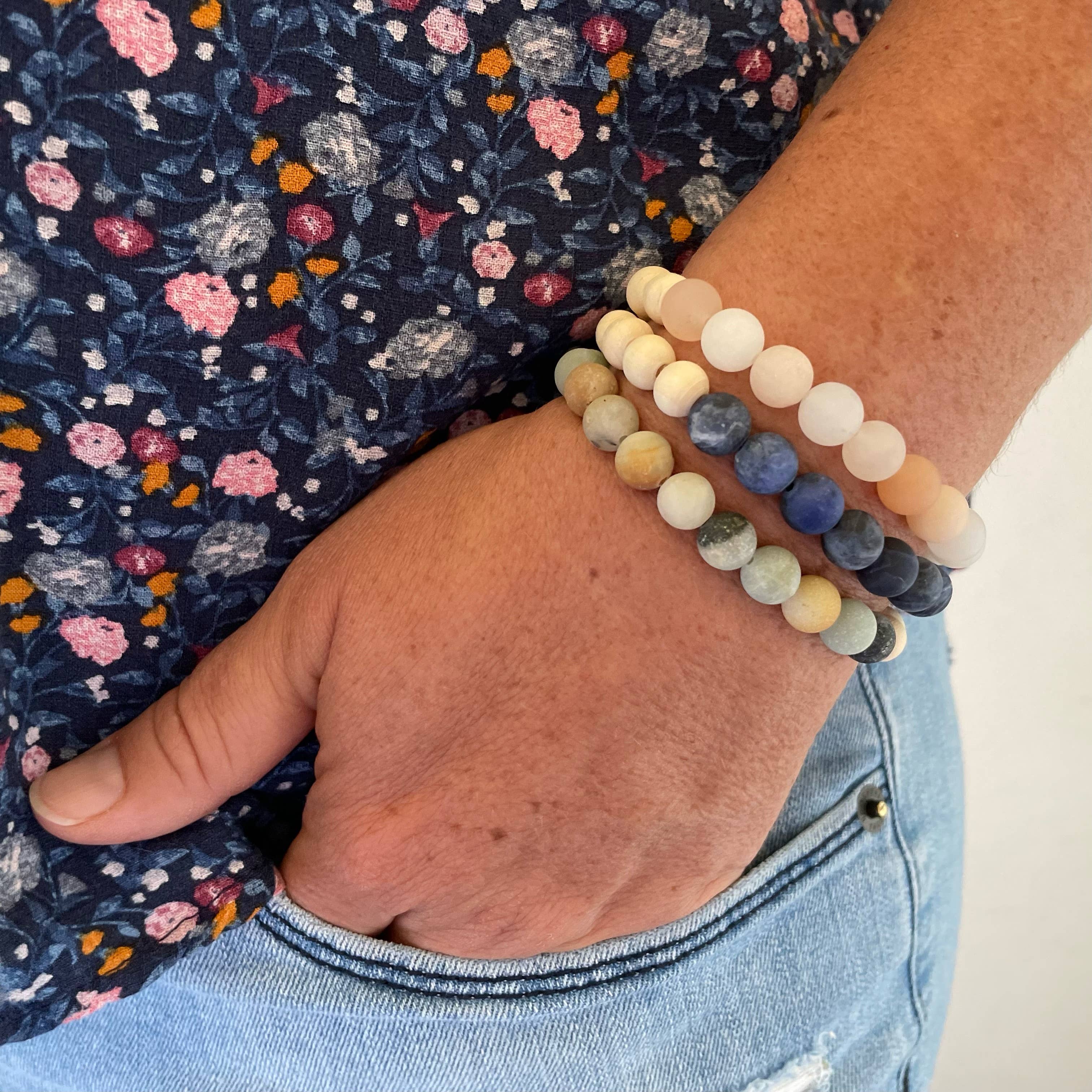 Hand wearing a stack of colorful beaded bracelets on a floral fabric background
