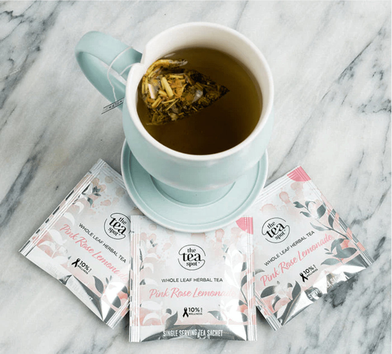 Tea cup with a tea bag and pink tea packages on a marble surface