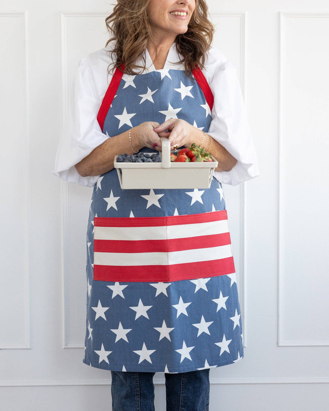 Person wearing an American flag apron holding a tray of berries.