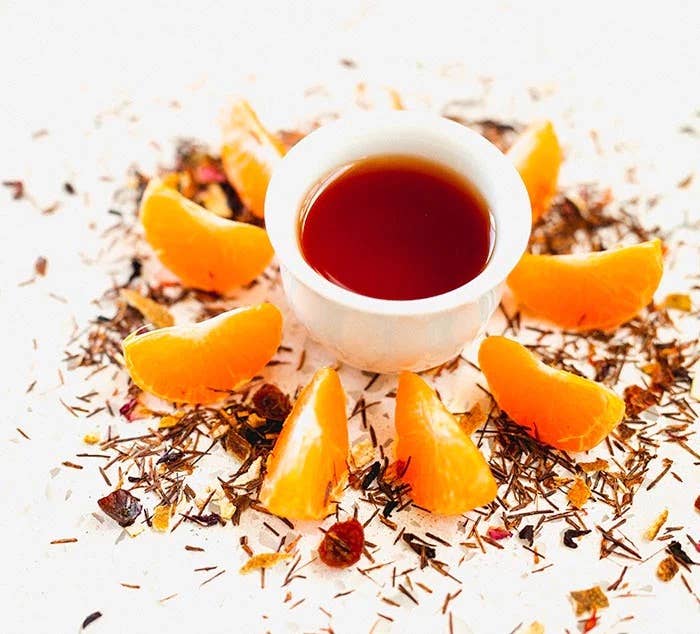 Tea cup with orange slices and dried herbs on a white background