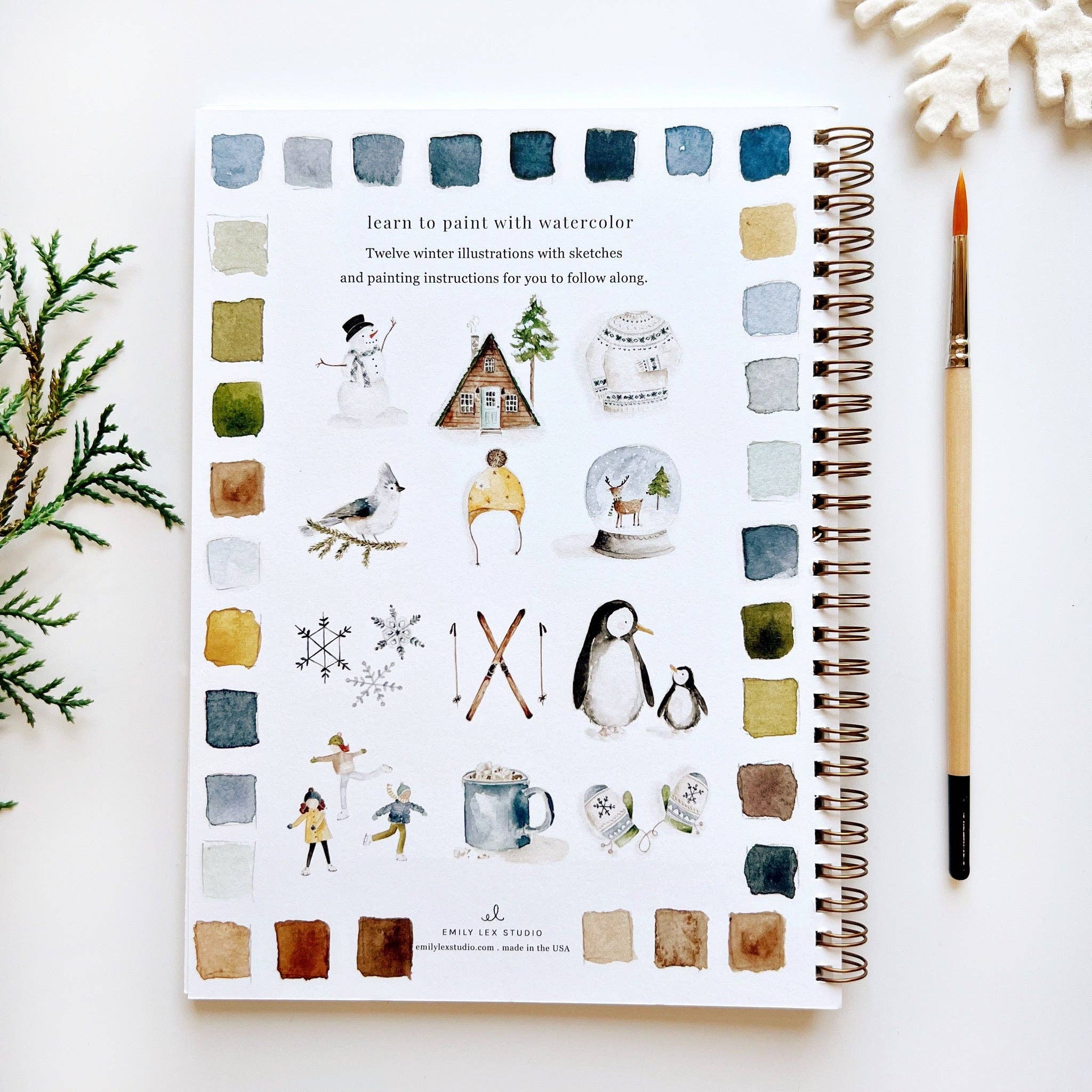 Notebook with watercolor illustrations on a white surface with a paintbrush and decorative elements.