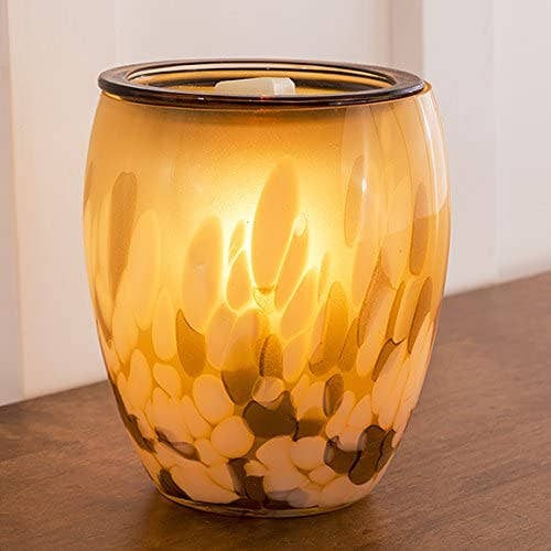 Glass wax melt warmer with a warm glow on a wooden surface