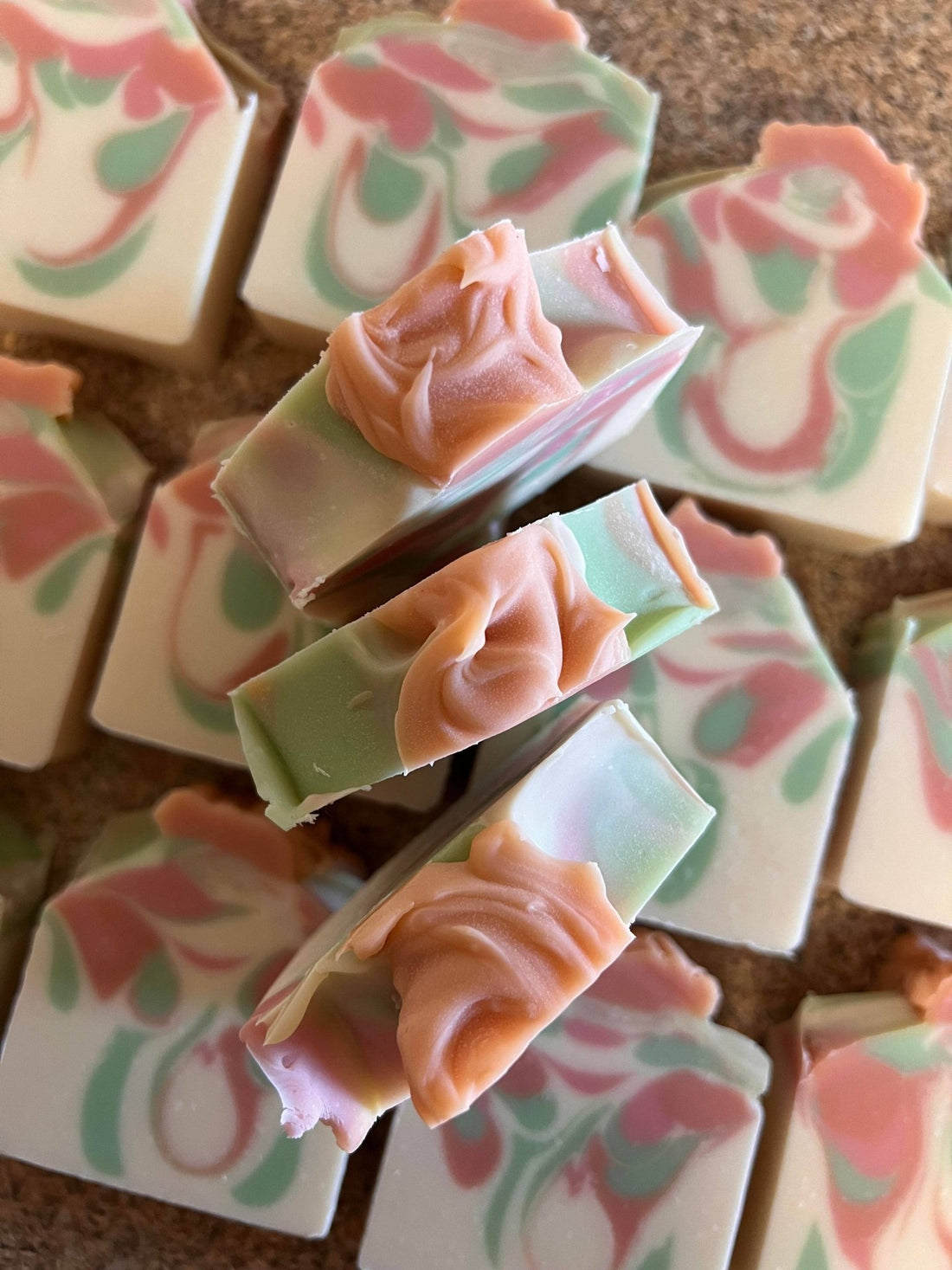 Decorative soap bars with floral designs in pink, green, and white on a brown surface.