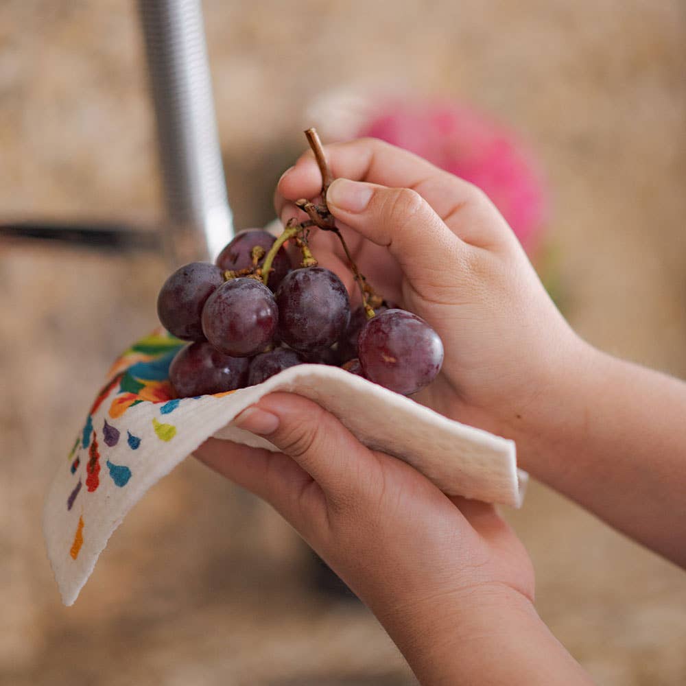 Hands holding a bunch of grapes wrapped in a colorful cloth against a blurred background
