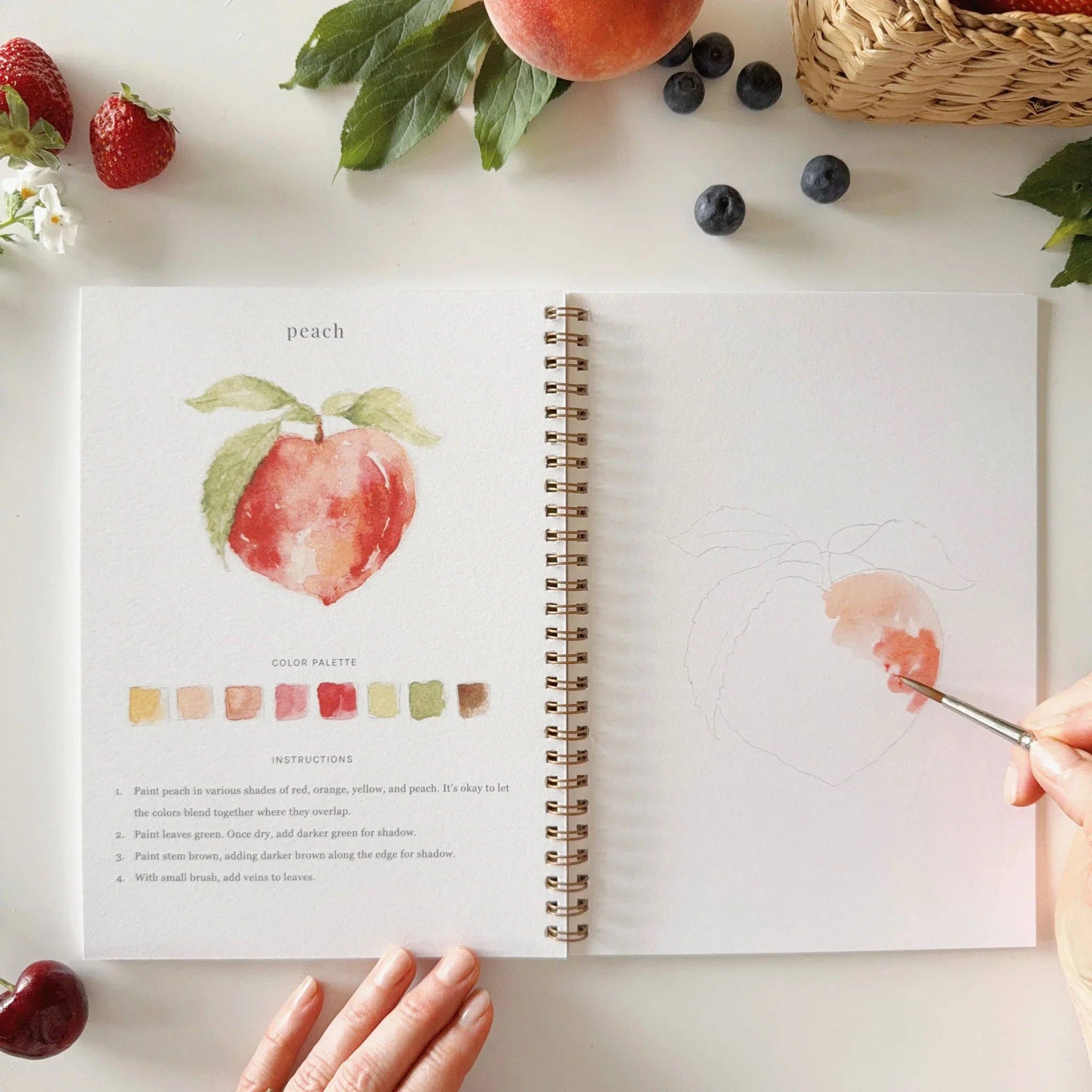 Open book with color palette and painting guide for peach, surrounded by fruits and a hand holding a paintbrush.