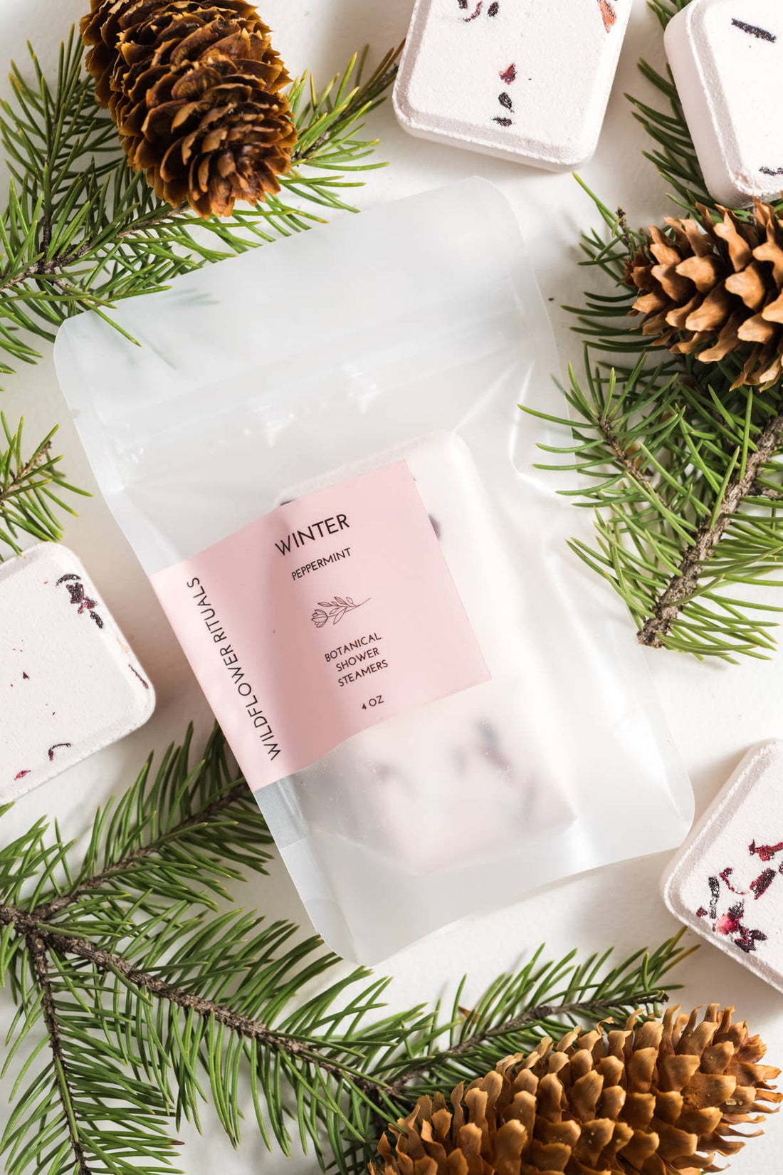 Product packaging with a pink label surrounded by pine branches and cones on a white background