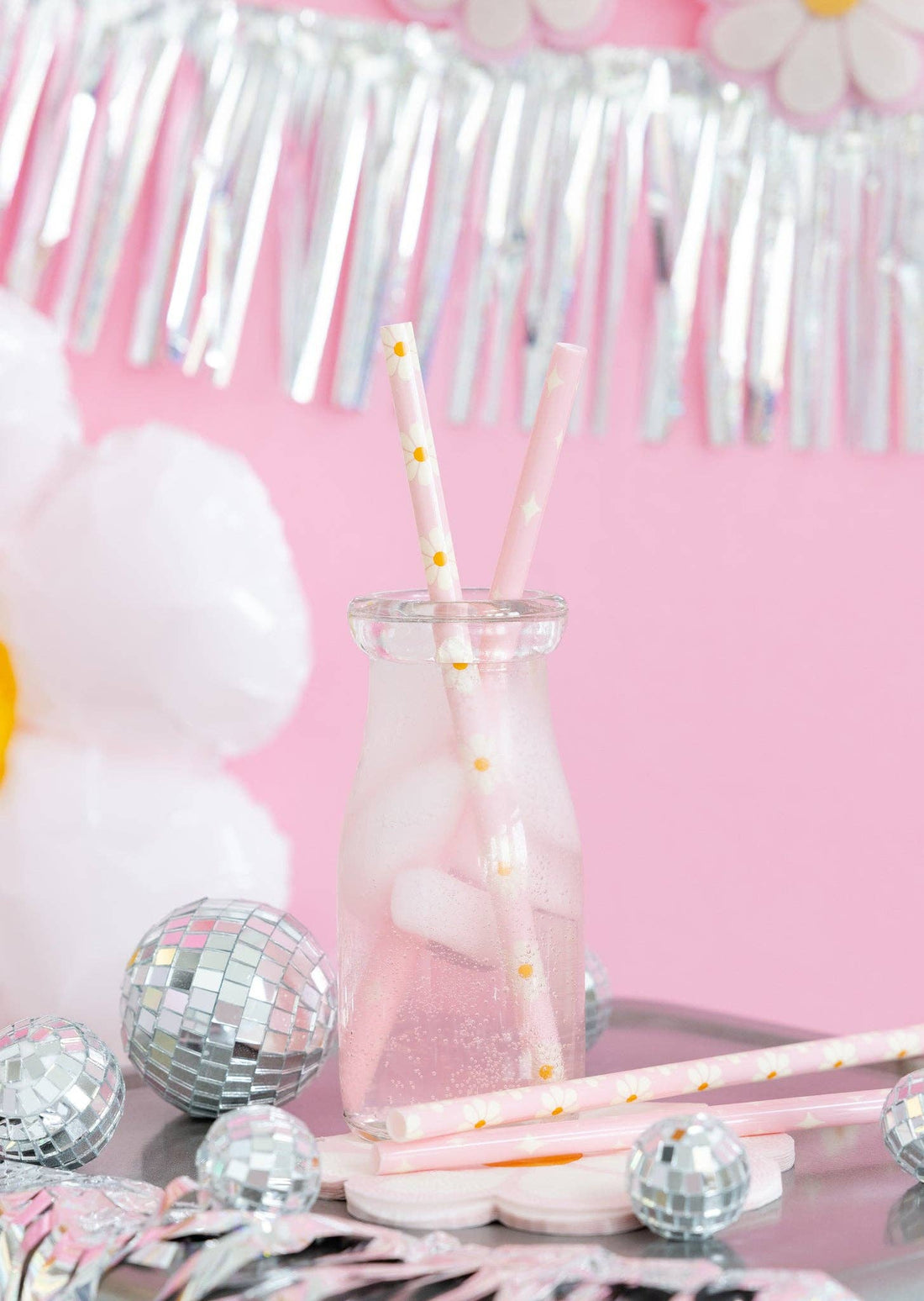 Glass with pink liquid and straws on a table with decorative items against a pink background