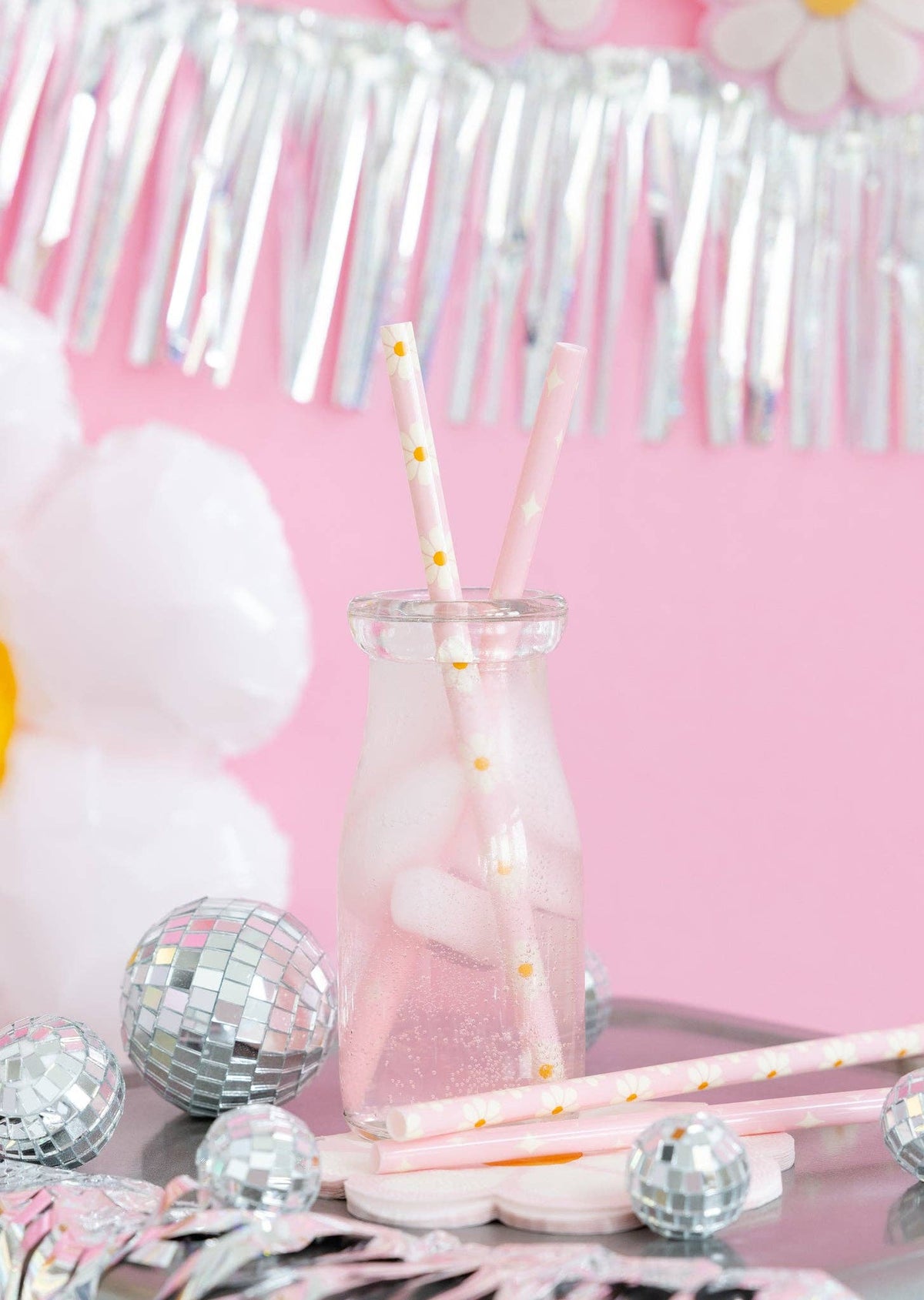 Glass with pink liquid and straws on a table with decorative items against a pink background