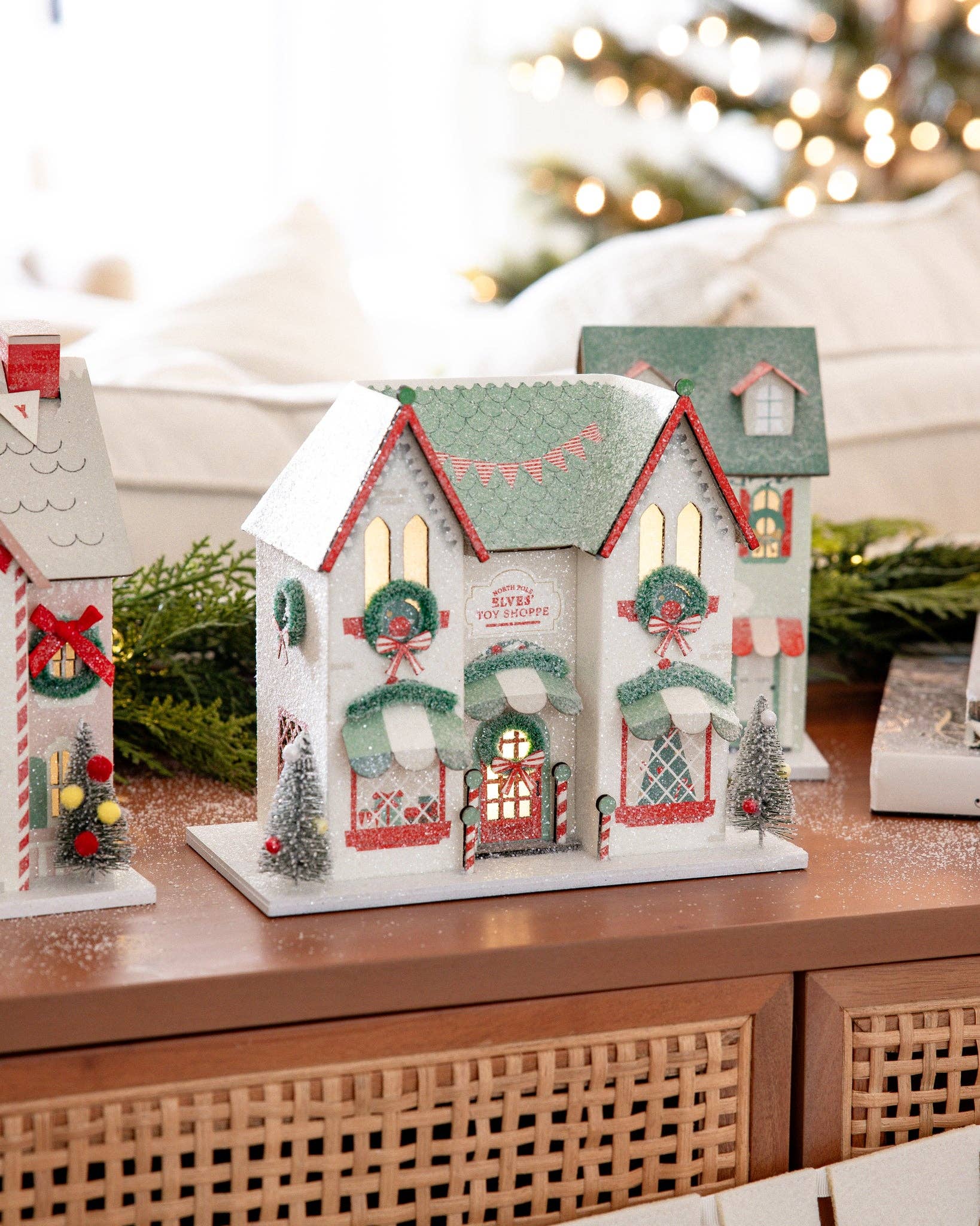 Decorative Christmas houses on a wooden surface with blurred lights in the background