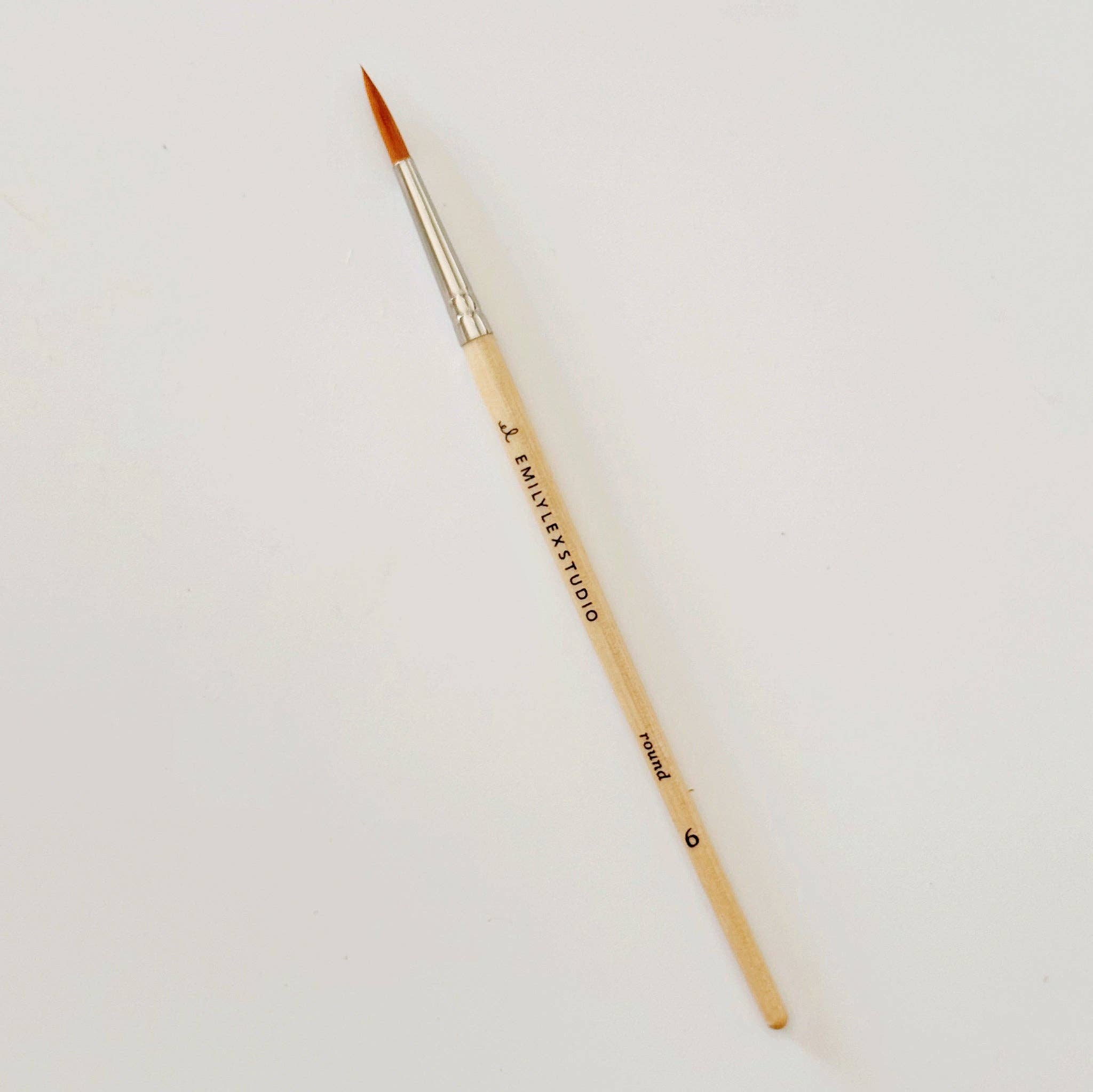 Paintbrush with wooden handle and gold ferrule on a light gray background