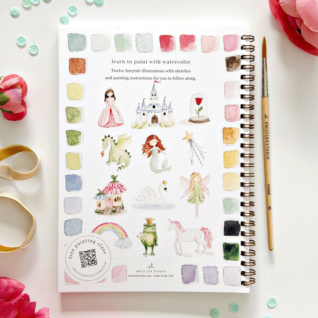 Watercolor art book with illustrations of fairies, castles, and other fantasy elements on a white surface with flowers and a pen.