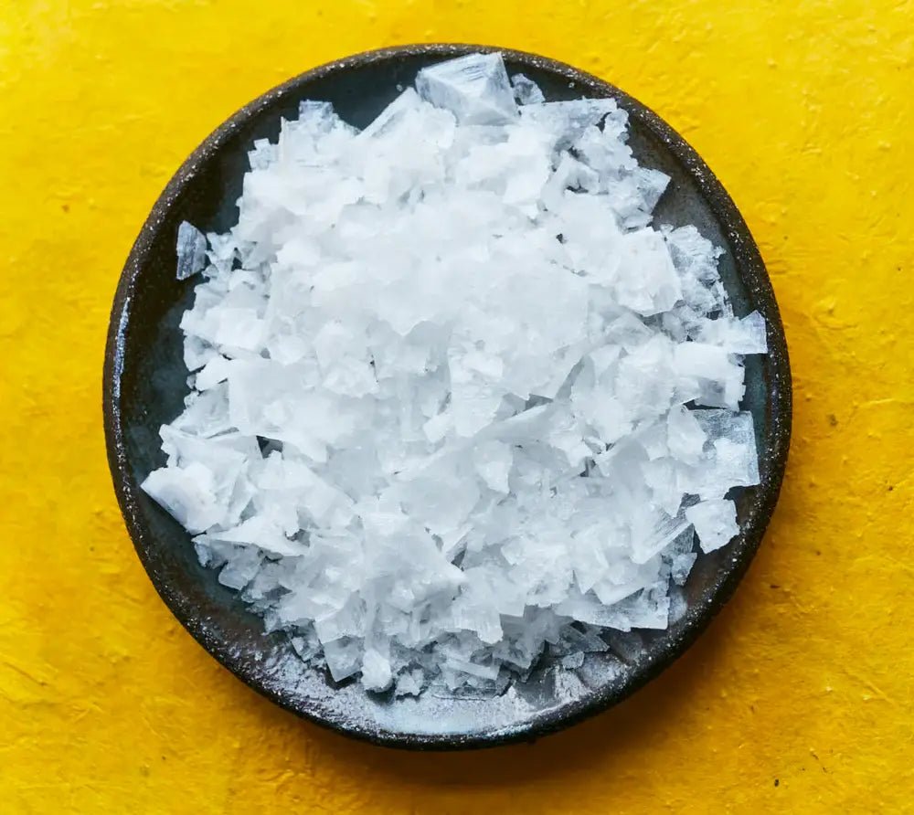 Coarse salt in a black bowl on a yellow background
