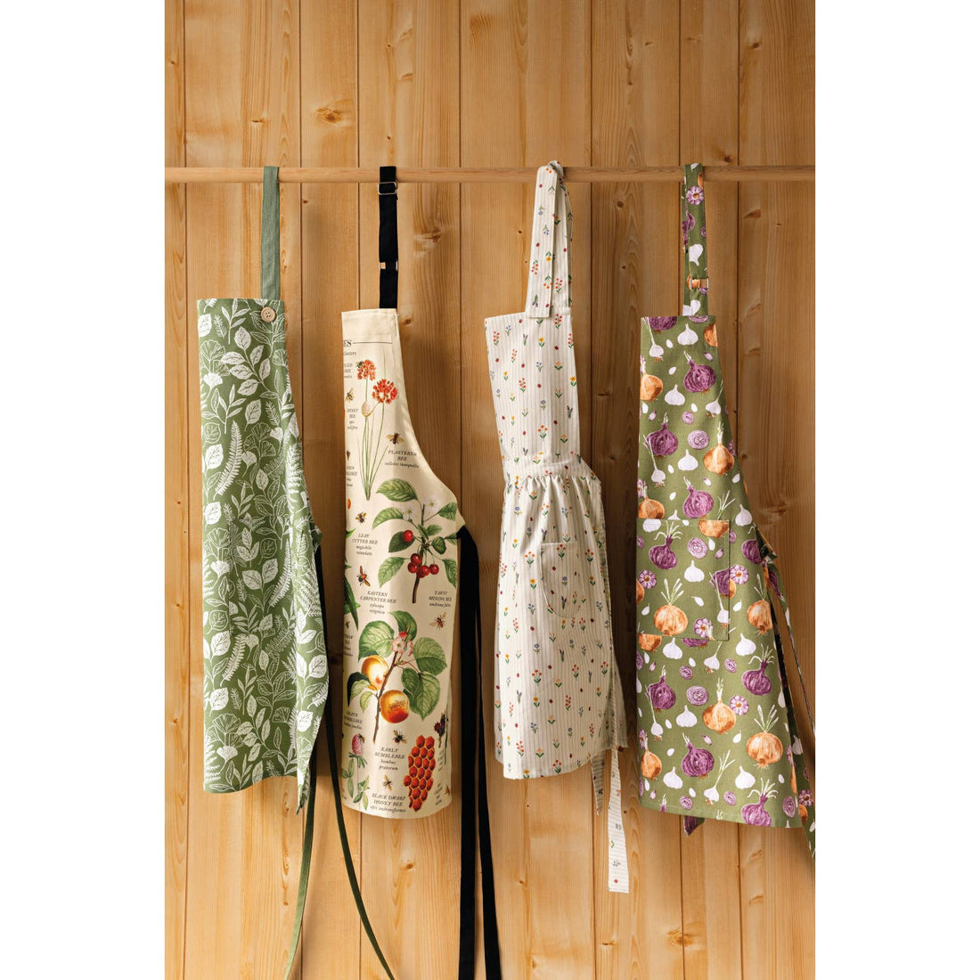 Four aprons with floral and nature-themed designs hanging on a wooden wall.