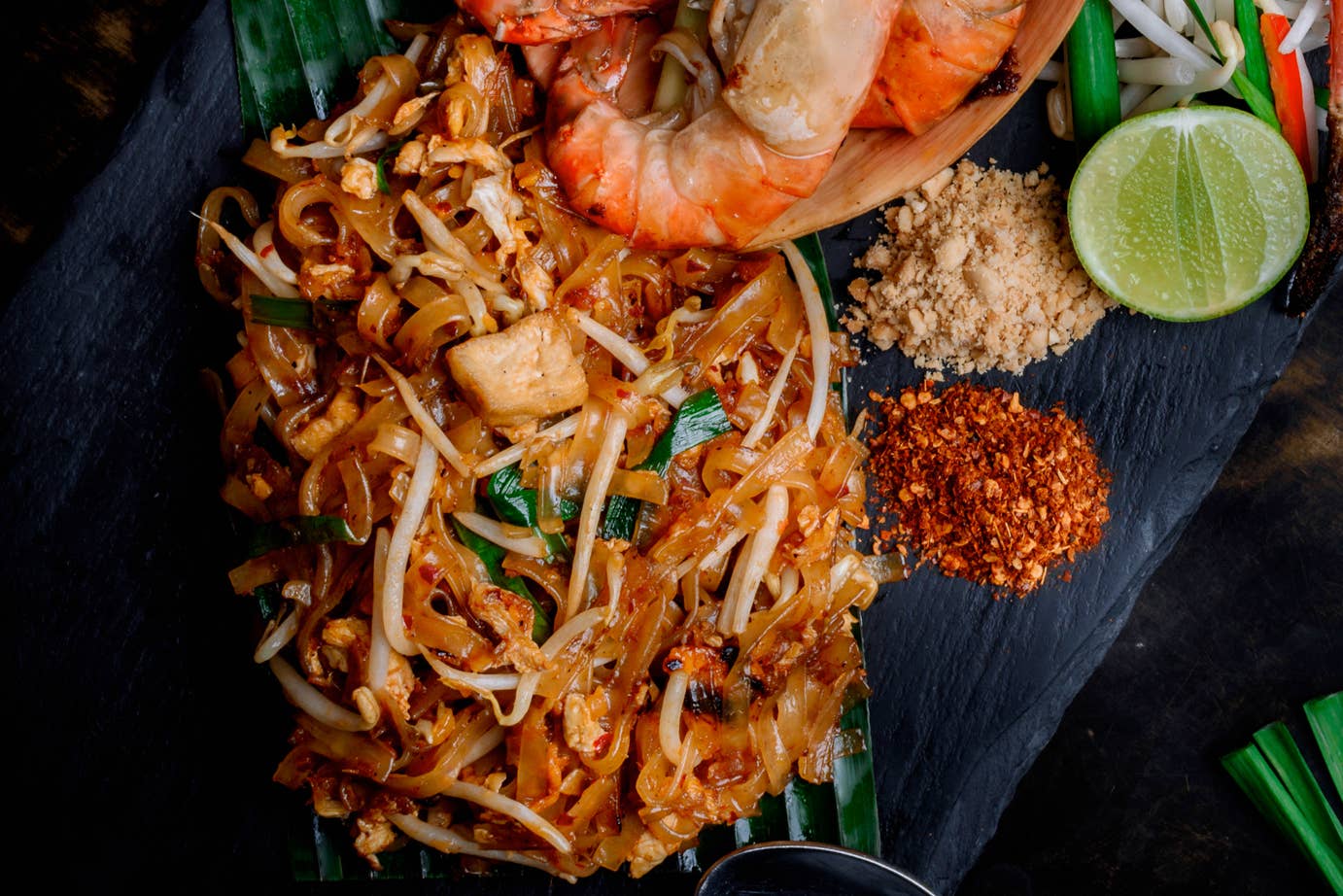 Plated dish of noodles with shrimp and garnishes on a dark surface
