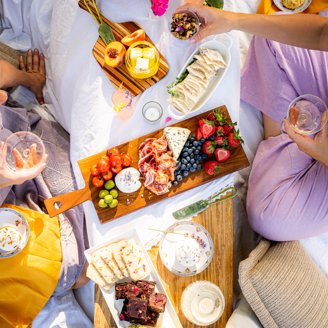 People enjoying a picnic with charcuterie board and drinks on a blanket.