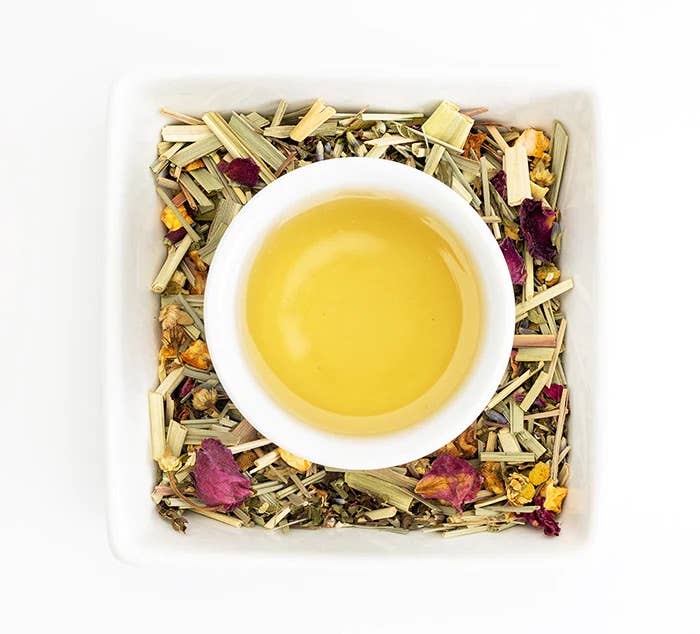 White cup of tea surrounded by dried herbs and flowers on a white background