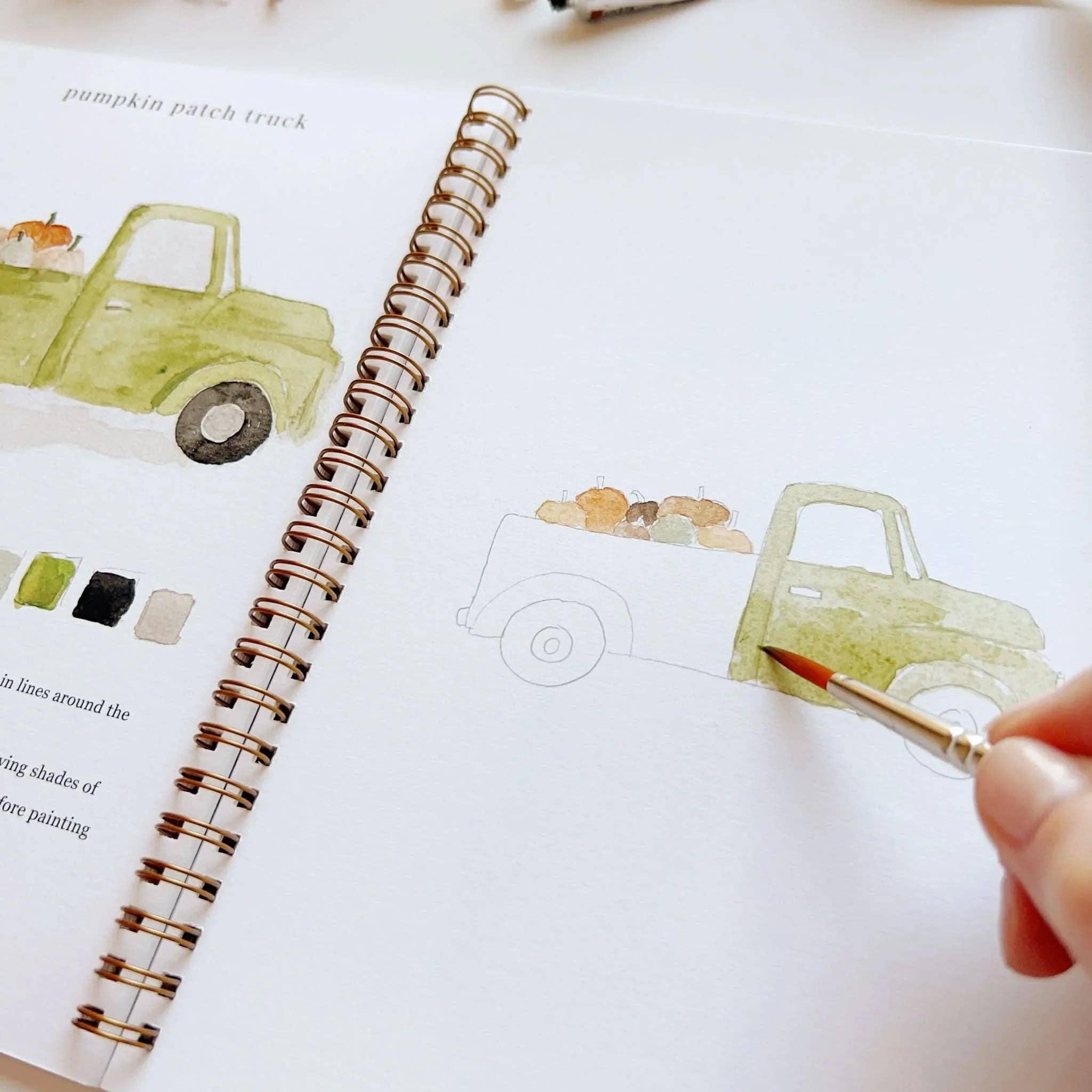 Person painting a watercolor truck on a notebook with a brush