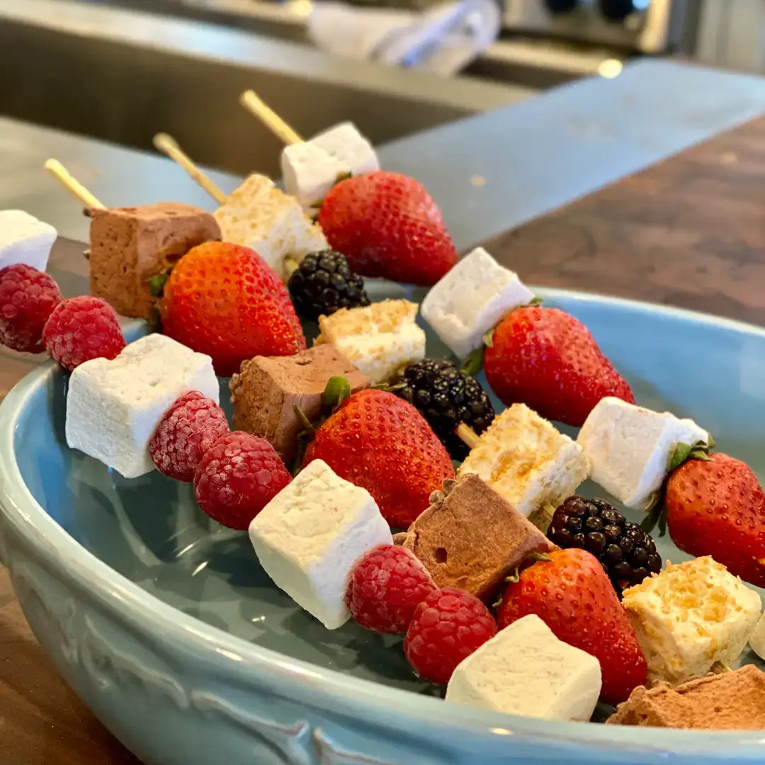 Dessert skewers with strawberries, marshmallows, and cookies on a blue plate.
