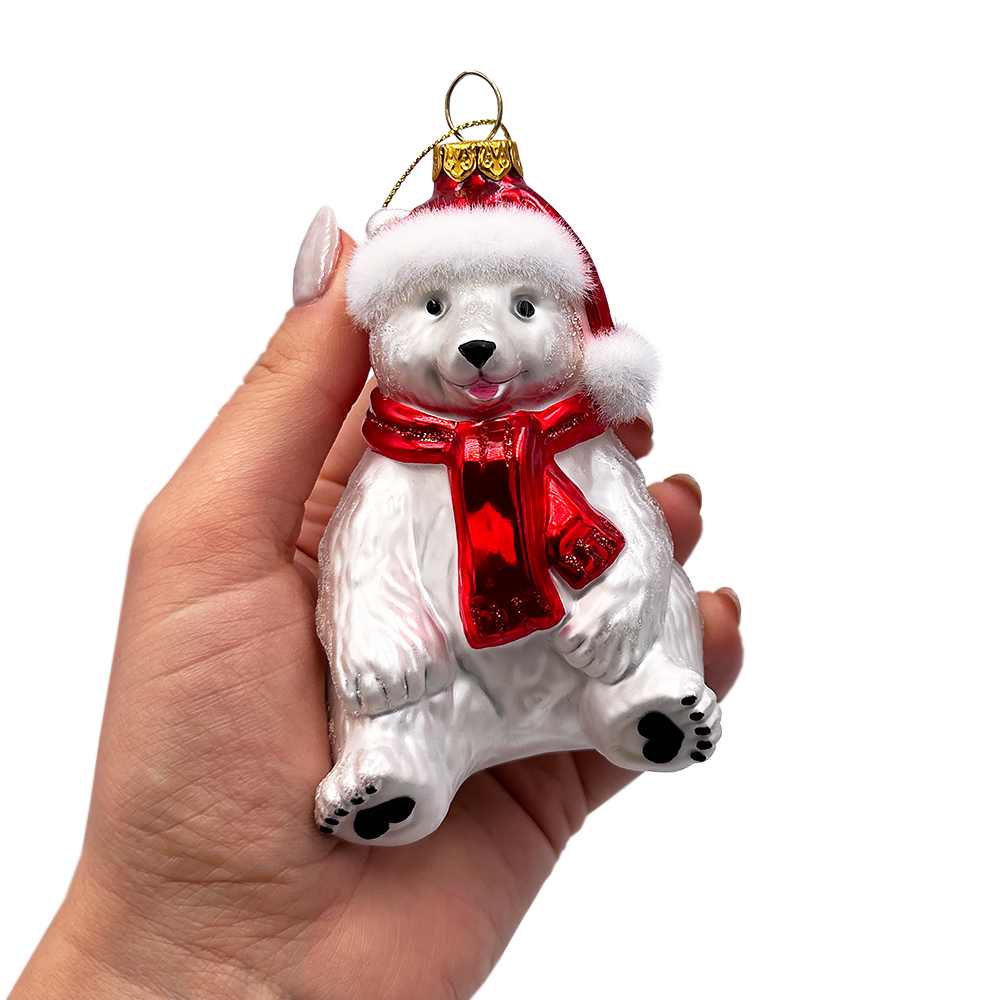 Glass polar bear ornament with red scarf and Santa hat held in a hand against a white background