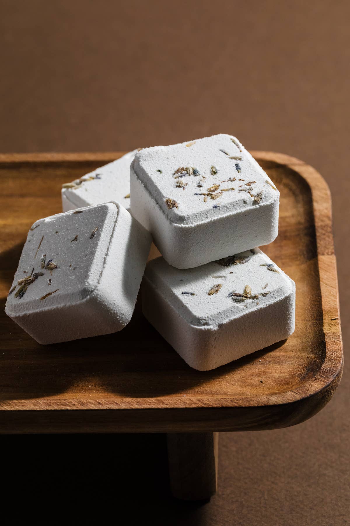 Four white shower steamers with herbs on a wooden tray against a brown background