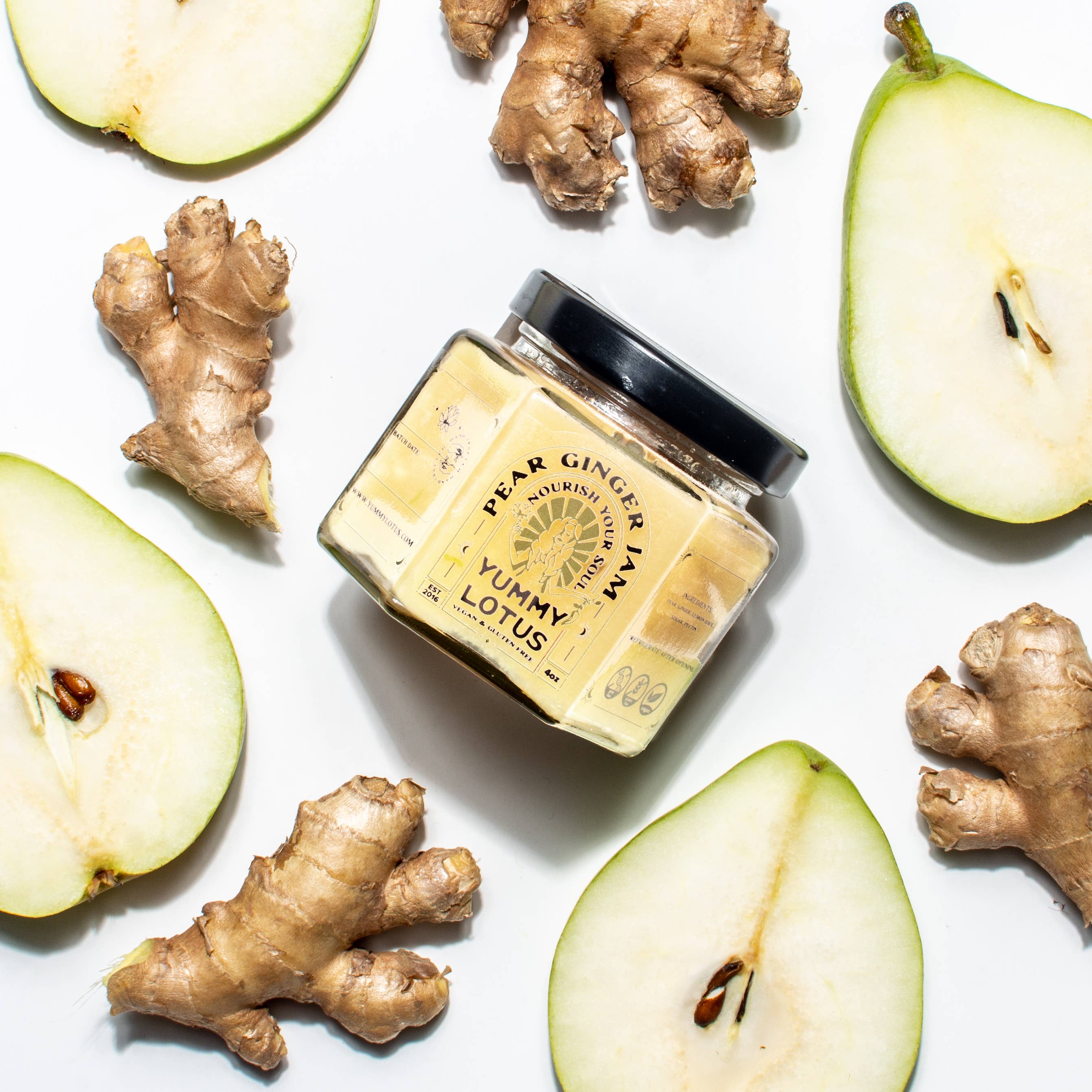 Jar of Yummy Lotus pear ginger spread surrounded by sliced pears and ginger roots on a white background