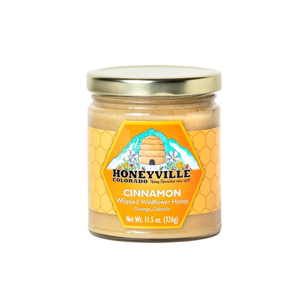 A jar of Honeyville Colorado Cinnamon Whipped Wildflower Honey with a gold lid and orange label, set against a plain white background.