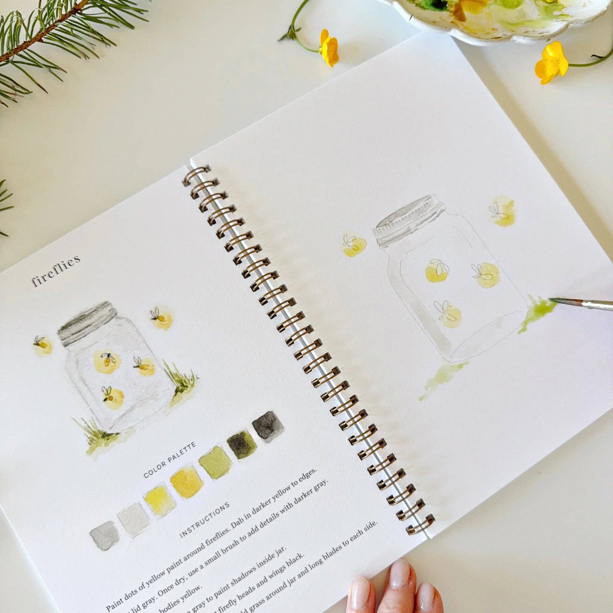 Open book with illustrations of jars and color palettes on a light surface.