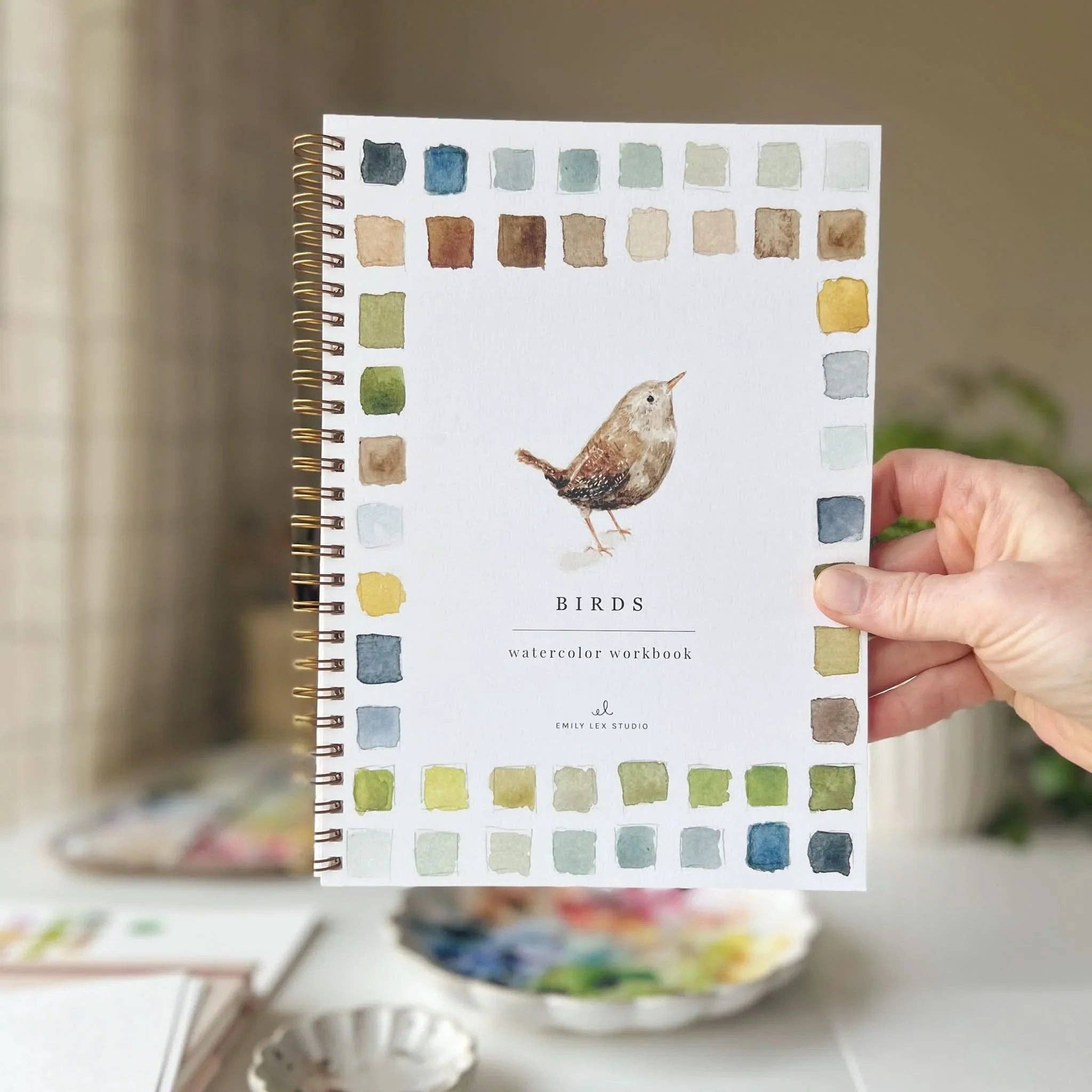 Notebook with bird illustration and color swatches held by a hand on a blurred background