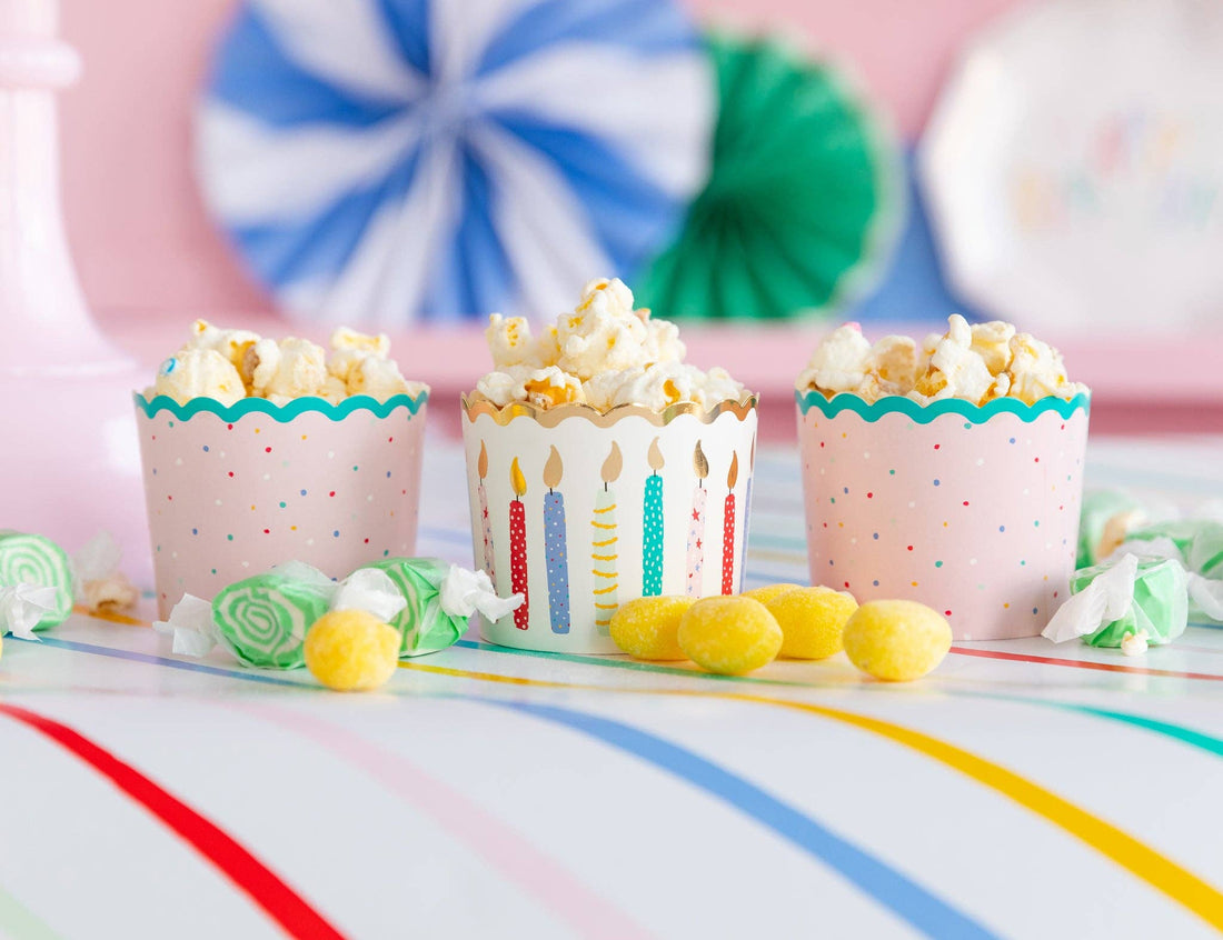 Three popcorn cups with colorful designs on a table with candy and party decorations.