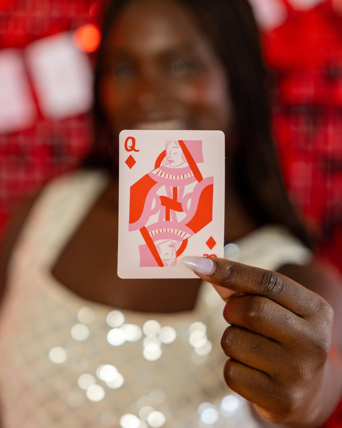 Person holding a Queen of Diamonds card against a blurred background