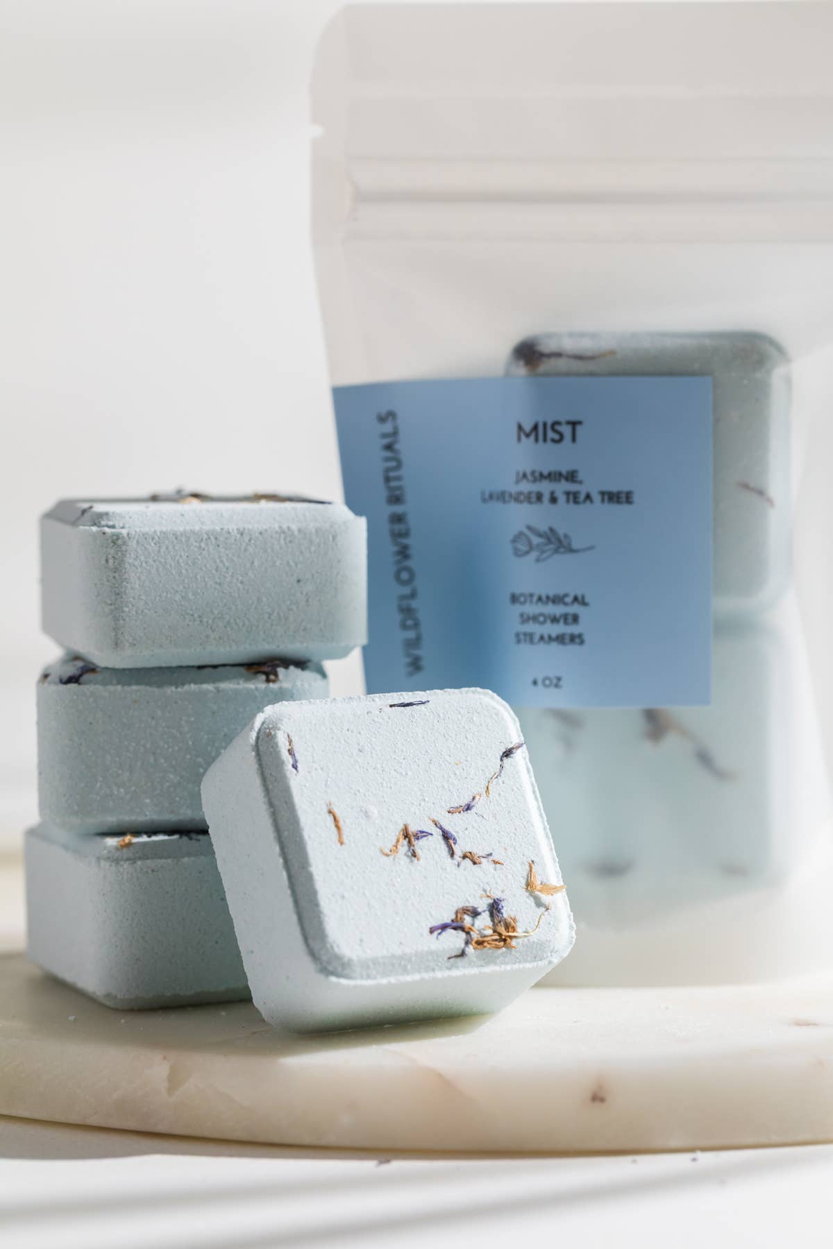 Three square bath bombs with a packaging bag labeled &