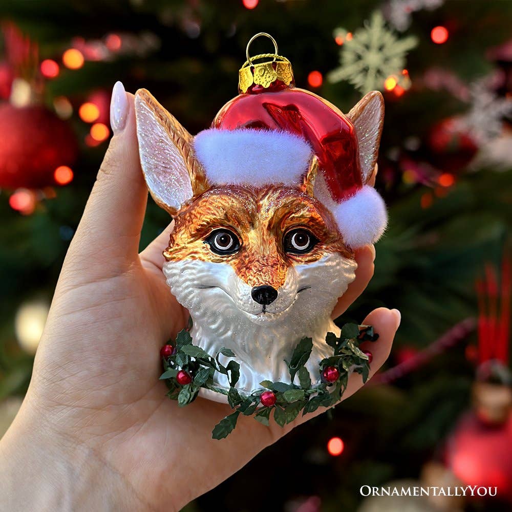 Hand holding a fox ornament with a Santa hat against a Christmas tree background