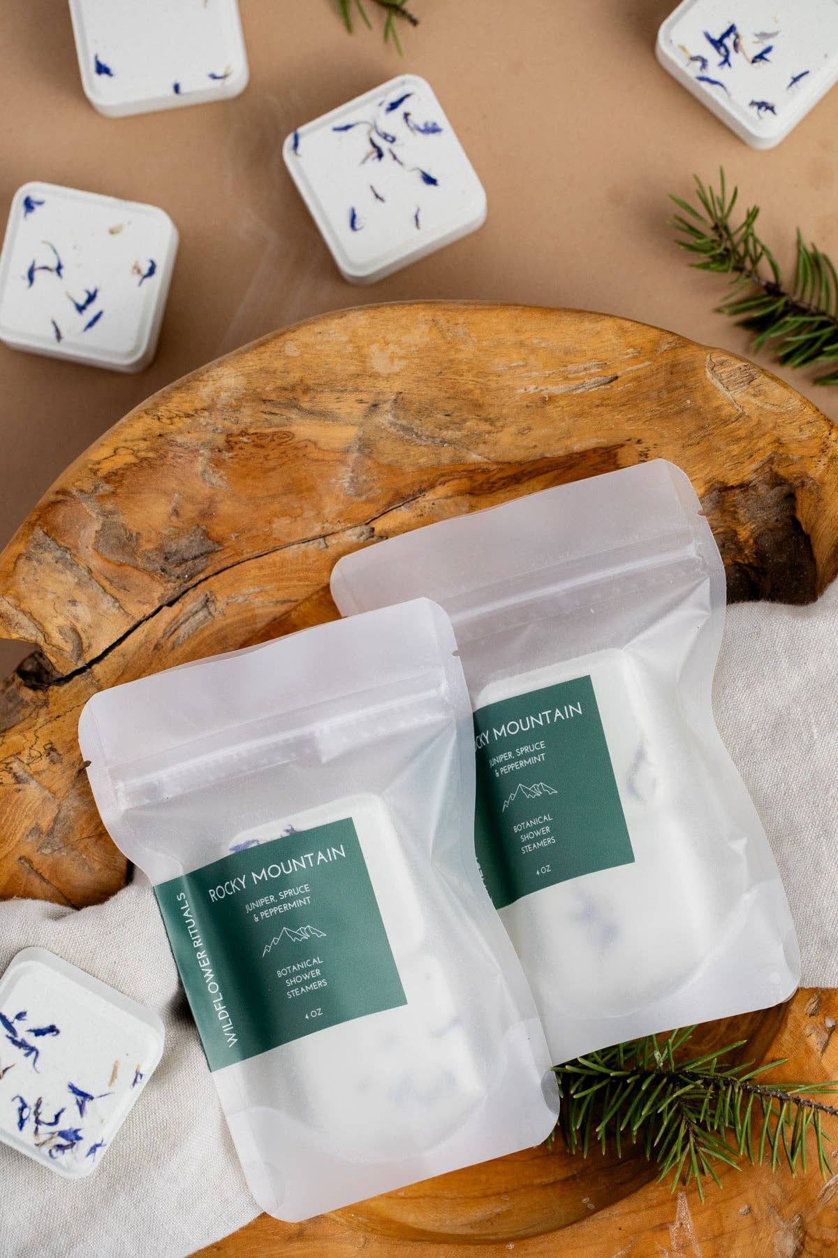 Two packages of Rocky Mountain tea on a wooden surface with loose tea leaves.