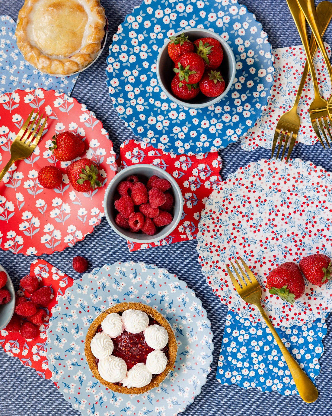 Dessert table with floral-patterned plates, bowls of berries, and pastries on a blue tablecloth.