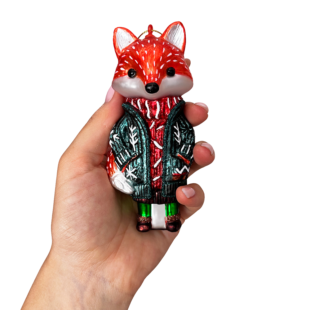 Hand holding a decorative fox ornament wearing a sweater on a white background
