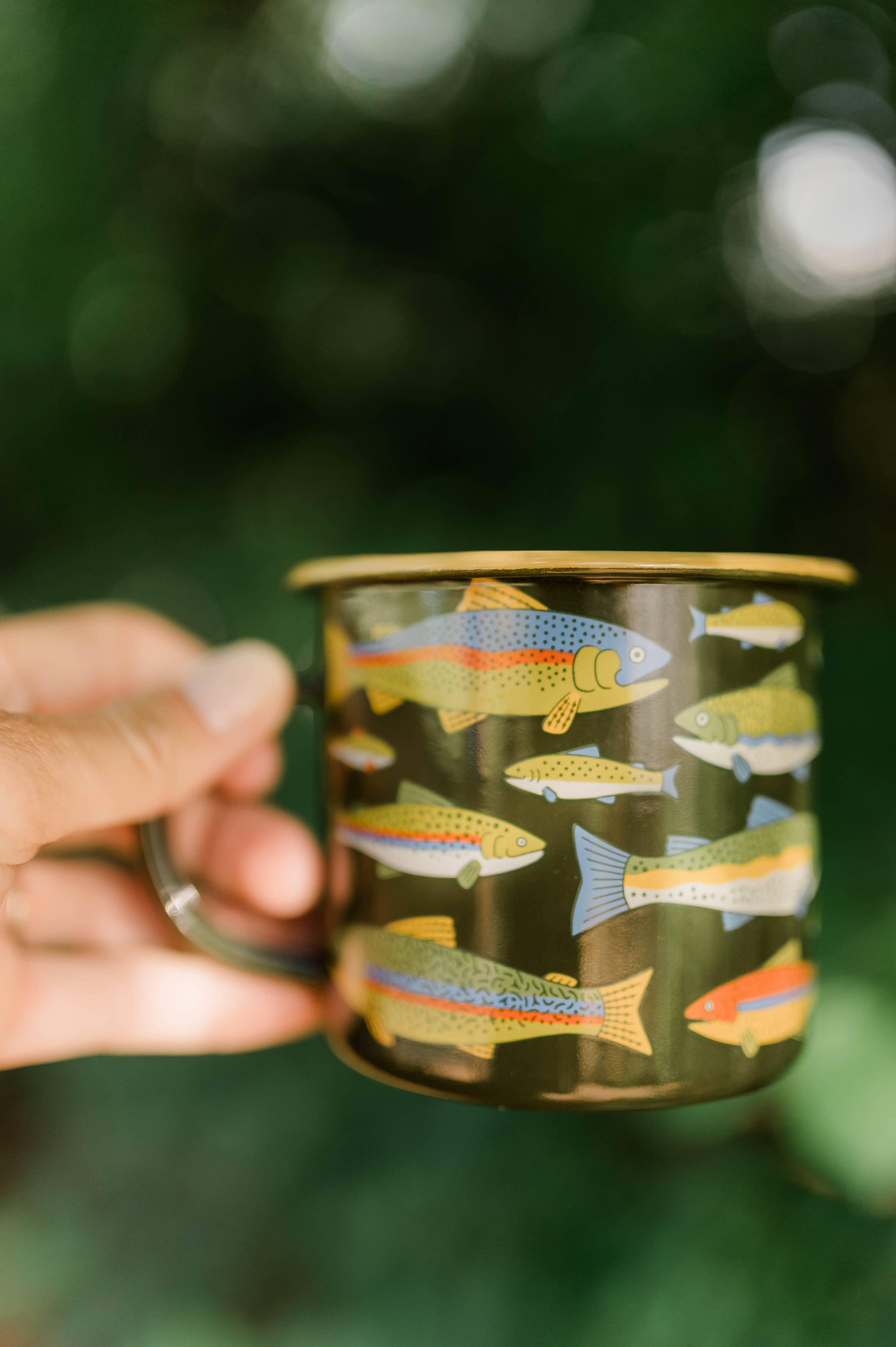 Hand holding a mug with fish design against a blurred green background