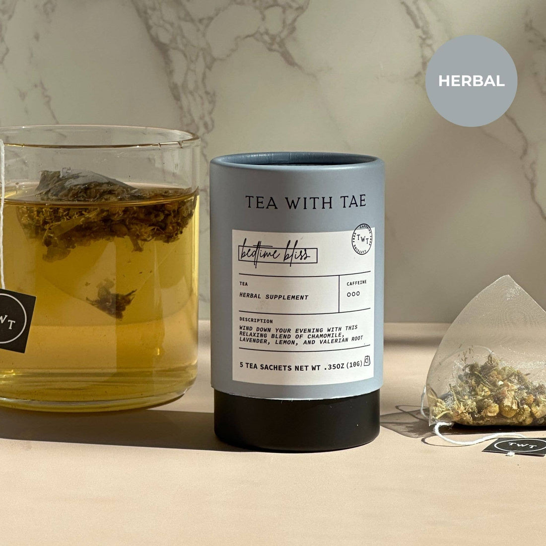Tea with Tae herbal tea canister next to a glass of tea and a teabag on a marble surface.