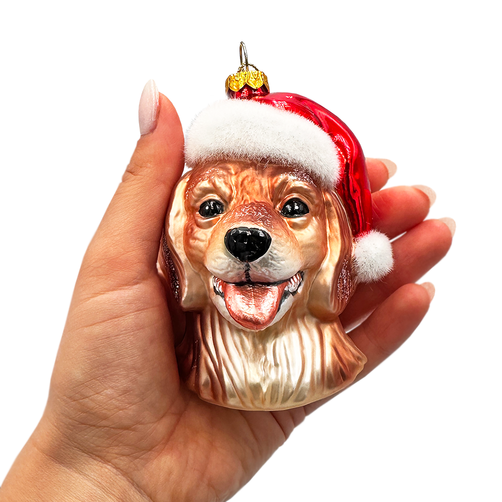 Dog-shaped Christmas ornament with a Santa hat held in a hand against a white background