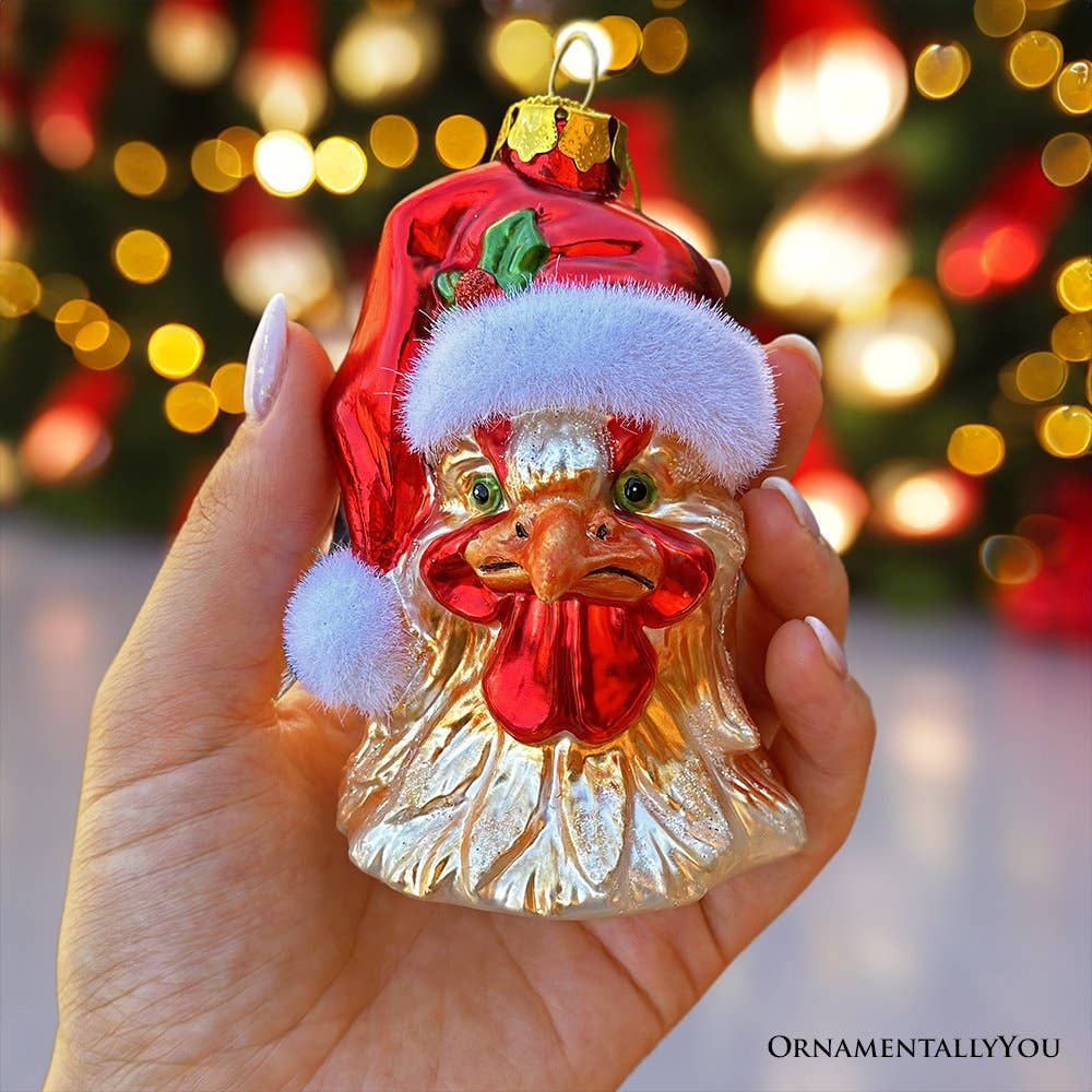 Decorative rooster ornament with Santa hat held in front of a blurred Christmas tree.
