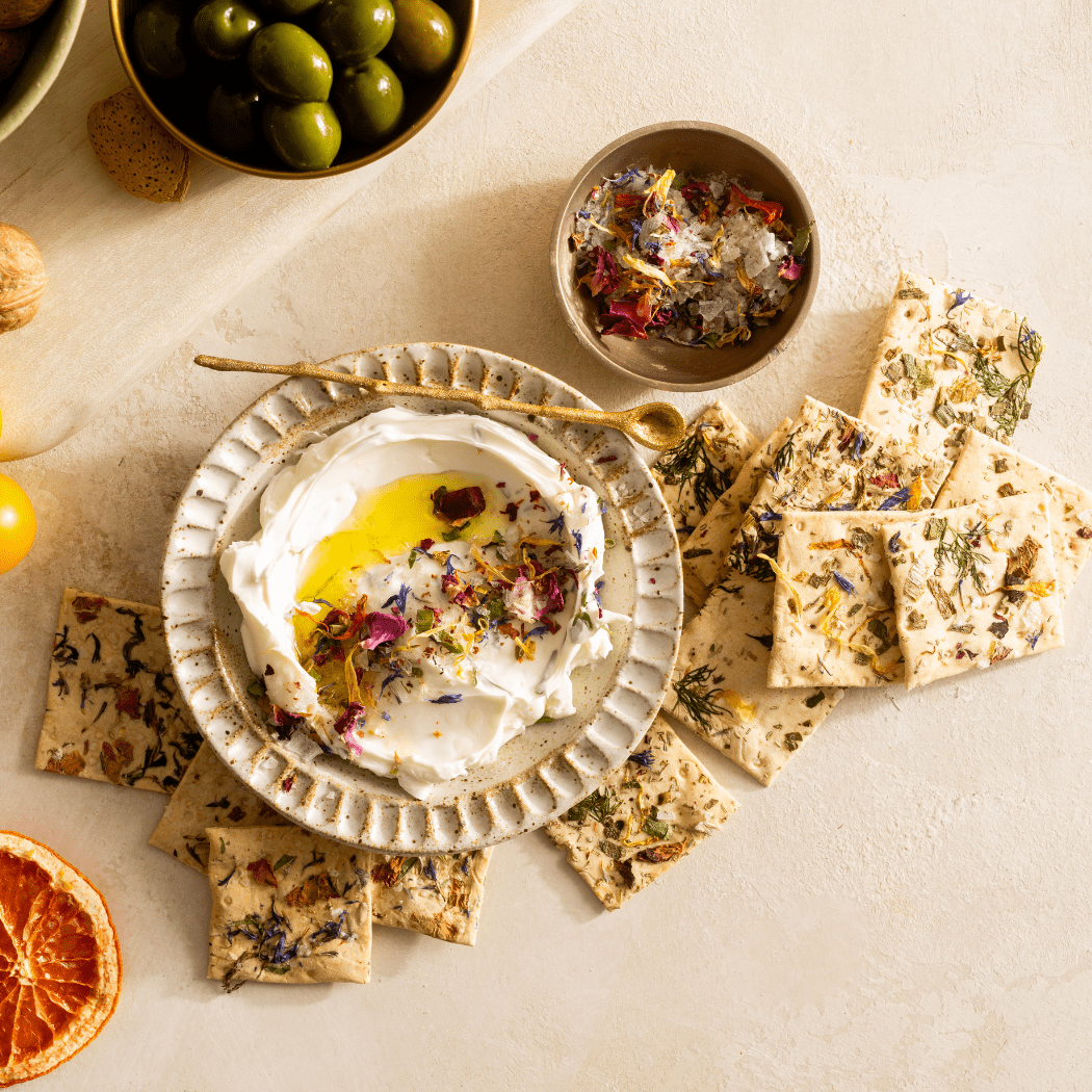 Dessert platter with a bowl of cream, crackers, and dried flowers on a light surface.