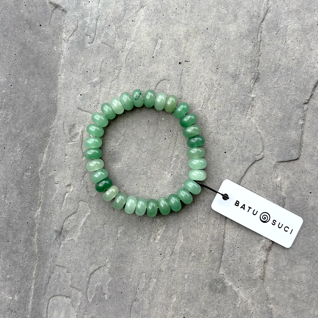 Green beaded bracelet on a textured gray background with a tag.