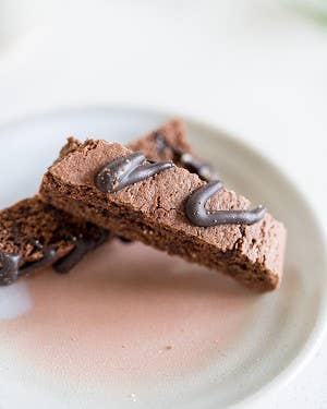 Two chocolate brownies with a glossy finish on a white plate.