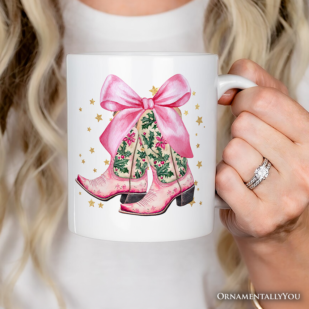 White mug with pink cowboy boots and a bow design held by a person.