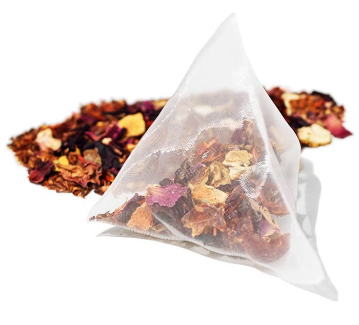 Triangular pyramid of tea bags with visible dry leaves and herbs on a white background