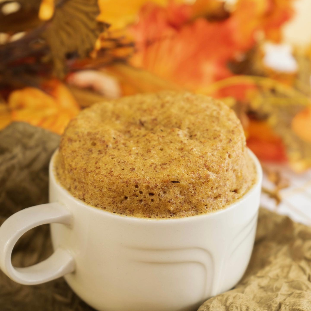 Cake in a white mug with autumn leaves in the background