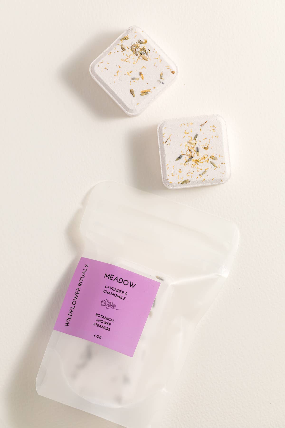 Two square shower steamers with decorative elements on a white background, accompanied by a purple label.