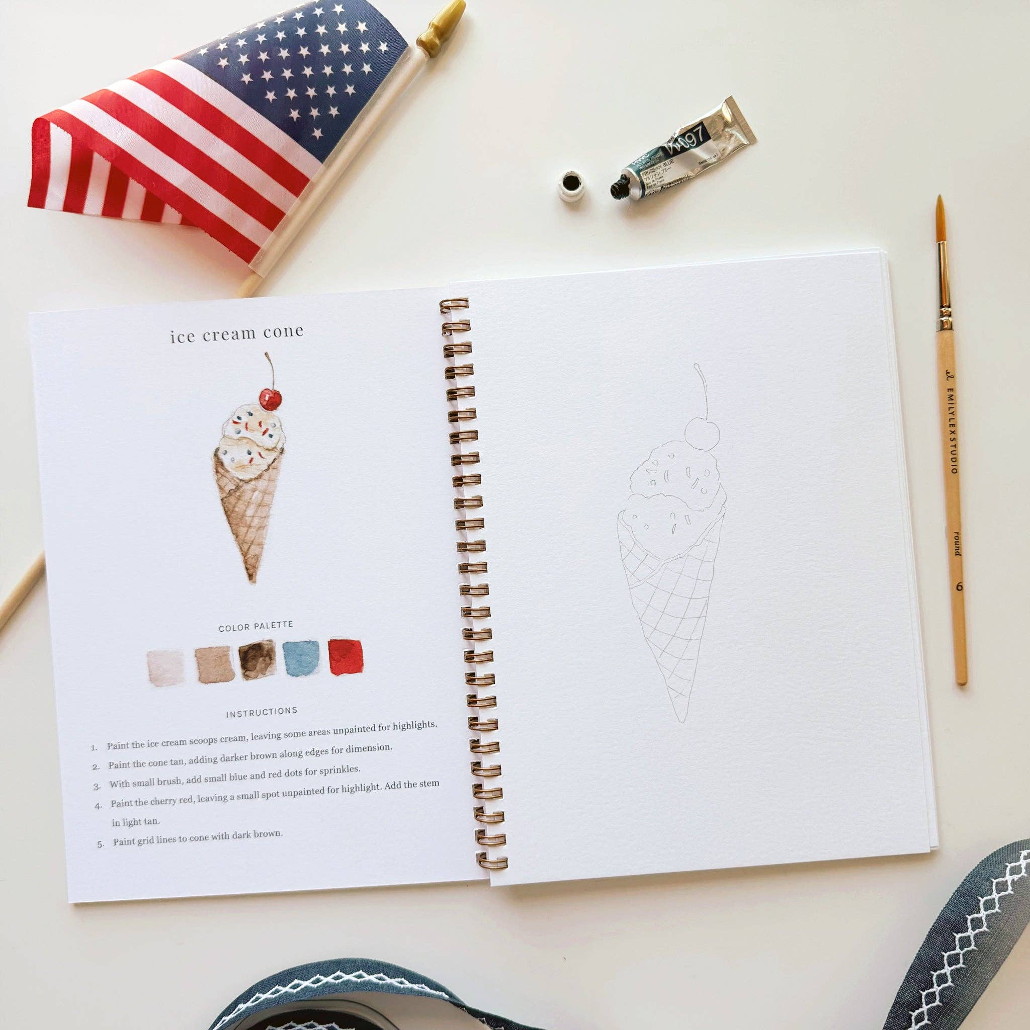 Open book with an illustration of an ice cream cone on a table with art supplies